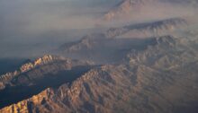 Luftaufnahme aus einem Flugzeug auf eine Gebirgskette mit Küste und Meer