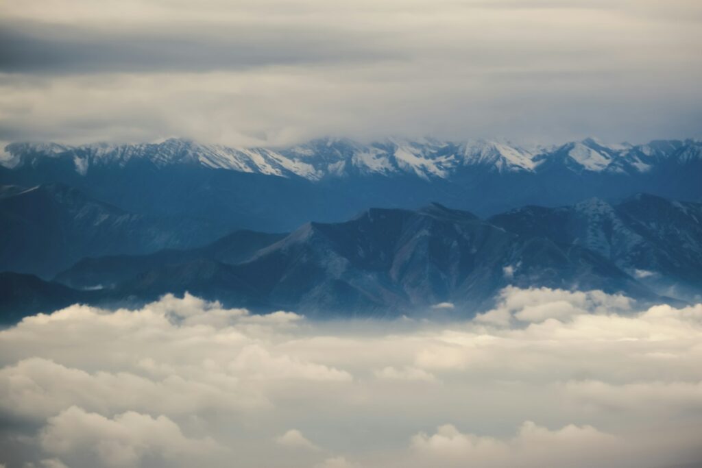 Blick aus einem Flugzeug auf die schneebedeckten Alpen, die zwischen weichen Wolken aus dem Dunst ragen