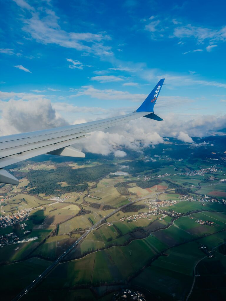 Blick aus einem Flugzeugfenster auf die Tragfläche über Feldern, Ortschaften und Wolken